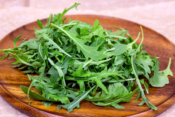Verse groene kruidige arugula salade bladeren op bruin houten plank op lichte achtergrond. - Foto, afbeelding