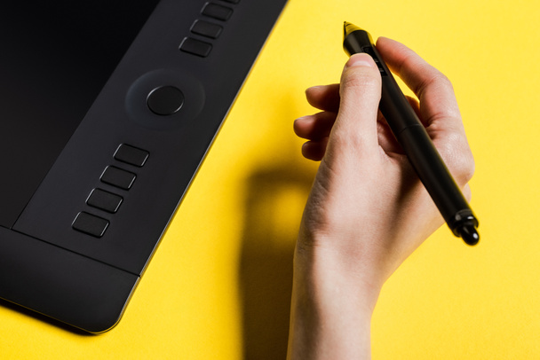 Cropped view of man holding stylus near graphics tablet on yellow surface - Foto, Imagem