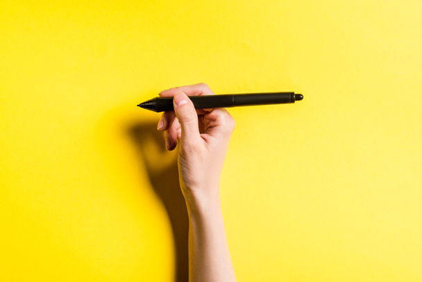 Vista recortada del diseñador sosteniendo lápiz de gráficos tableta sobre fondo amarillo
 - Foto, Imagen