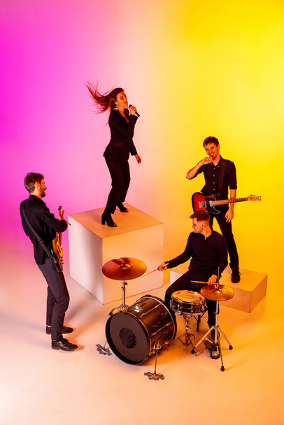 Young caucasian musicians, band performing in neon light on gradient studio background - Foto, imagen