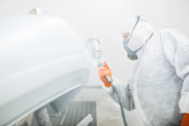 Male repairman painter in chamber painting automobile car elements. Worker paints the vehicle in white with a spray gun. - Foto, imagen
