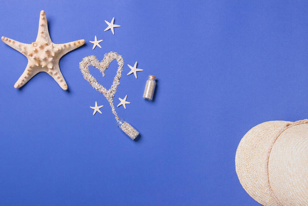 Coeur de sable de la bouteille, étoile de mer et chapeau de staw sur fond bleu, vue de dessus
. - Photo, image