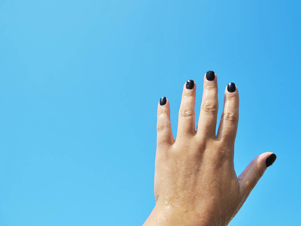 weibliche Hand mit schwarzen Nägeln auf Himmelshintergrund. - Foto, Bild