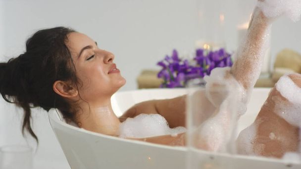 Крупный план расслабленной женщины мыть руки в пенной ванне. Горячая девушка отдыхает в ванной
. - Фото, изображение