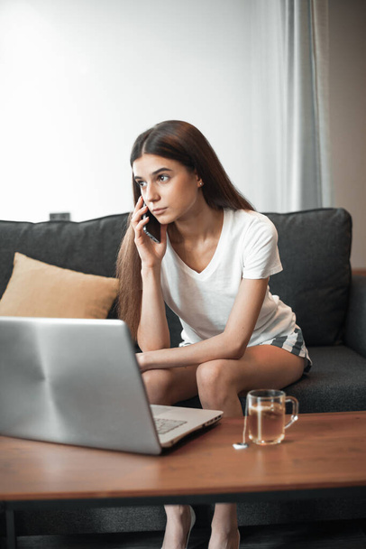 Молодая женщина с современным ноутбуком сидит дома на диване. Счастливая девушка, просматривающая Интернет в свободное время..  - Фото, изображение