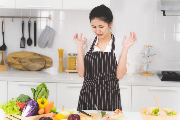 Молодая азиатская женщина или домохозяйка устала от приготовления пищи, которая состоит из различных фруктов и овощей для семьи
. - Фото, изображение