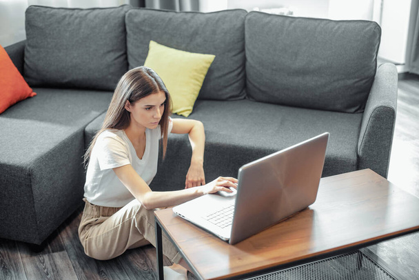 Young woman with modern laptop sitting on sofa at home. Happy girl browsing through the internet during free time..  - Fotografie, Obrázek