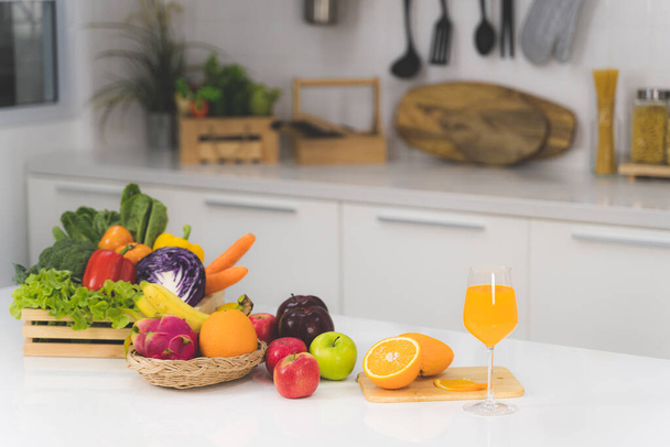 Un vaso de jugo de naranja y una rebanada de naranja con muchas verduras y frutas en una mesa blanca en la cocina
 - Foto, imagen