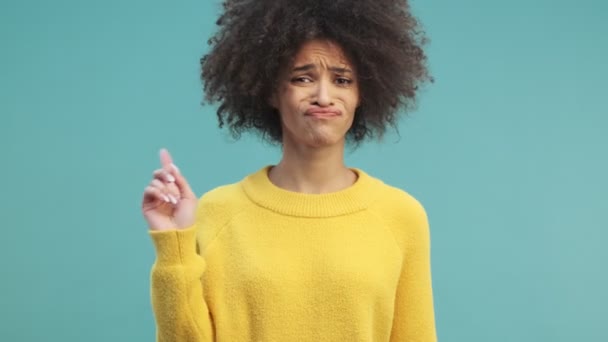 A disappointed young african american woman with curly hair is showing NO gesture with raised finger isolated over blue wall background in studio - Кадри, відео