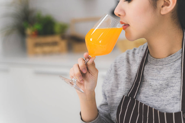 Zamknij się piękna azjatycka kobieta, gospodyni domowa z sokiem pomarańczowym w białej kuchni z dużą ilością świeżych warzyw i owoców na stole. - Zdjęcie, obraz