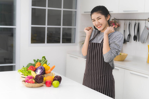 美しいアジアの女性の肖像画、主婦はテーブルの上に新鮮な野菜や果物がたくさんある白いキッチンで非常に満足しています. - 写真・画像