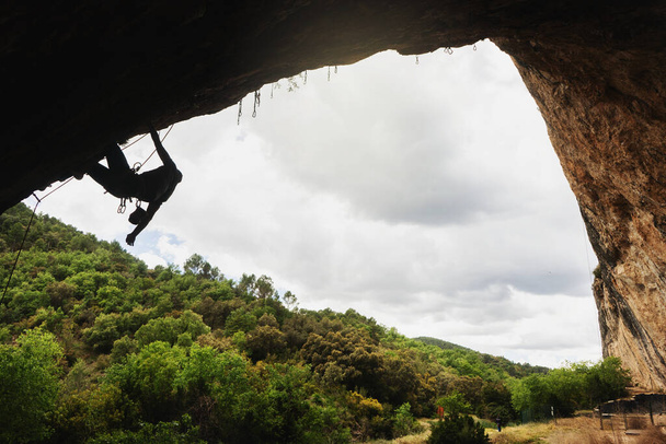 Mağaranın içindeki çökmüş bir duvara tırmanan genç bir adamın silüeti. Bulutlu gökyüzü arkaplanı. - Fotoğraf, Görsel