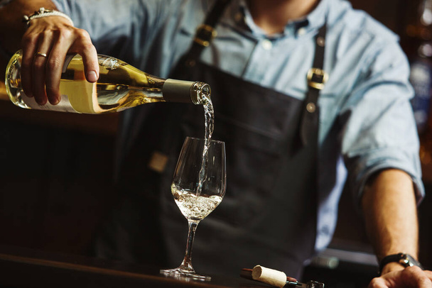 Male sommelier pouring white wine into long-stemmed wineglasses. - Fotoğraf, Görsel