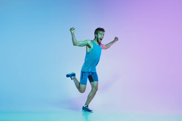 Full length portrait of active young caucasian running, jogging man on gradient studio background in neon light - Foto, afbeelding