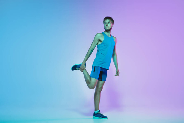 Full length portrait of active young caucasian running, jogging man on gradient studio background in neon light - Foto, immagini