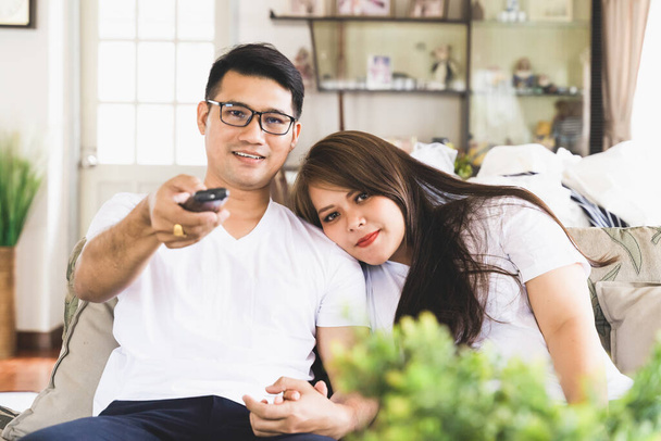 Asian male and female couples are watching TV on the sofa in the house. - Photo, image