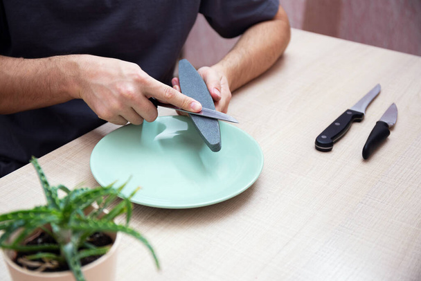 Close-up sterke mannelijke handen slijpen een keuken metalen mes met een slijpsteen. Thuis huishouden mes slijpen. - Foto, afbeelding