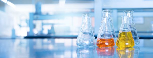 科学のオレンジ色の黄色の溶液ガラスのフラスコは青の研究化学実験室のバナーの背景を獲得 - 写真・画像
