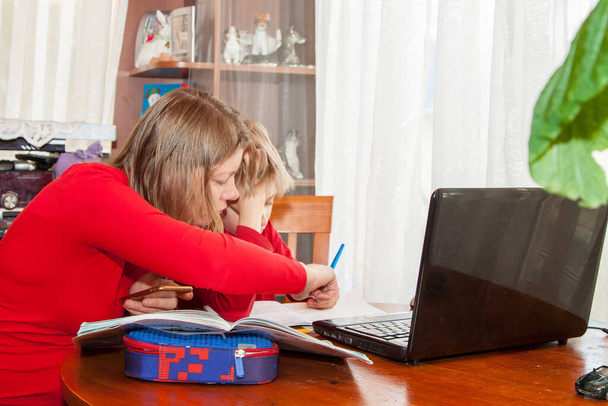 Child studying from home with help of mother taking remote class because of social distance. Mother helping her son with his homework or e-learning from home during Covid-19 pandemic lockdown - Zdjęcie, obraz