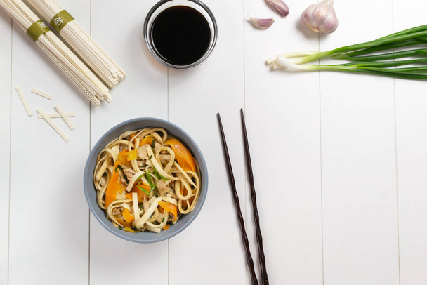 Udon noedels met kip, wortelen, groene uien, sojasaus en verse ingrediënten op een wit bord. Bovenaanzicht. Japanse keuken. Kopieerruimte. - Foto, afbeelding