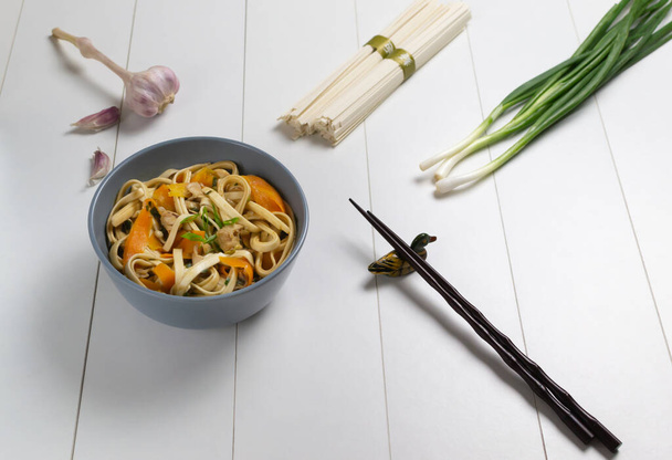 Udon-Nudeln mit Hühnchen, Karotten und grünen Zwiebeln und frischen Zutaten auf weißem Hintergrund. Japanische Küche. - Foto, Bild