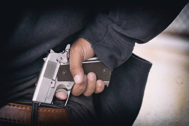 Close up gun in man's hand tucked at the back jeans. - Photo, Image