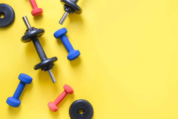 Sport colorful dumbbells on yellow background. View from above, copy space. - 写真・画像