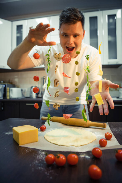 サラミキノコオリーブチーズのようなピザの材料を作る男が空気中で凍る。家庭料理 - 写真・画像
