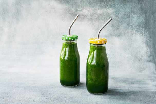 Groene smoothie met spinazie in twee kleine flesjes met metalen rietje op grijze ondergrond. Begrepen, ruimte. Gezond levensstijl concept. - Foto, afbeelding
