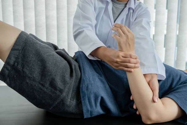 女性理学療法士は、リハビリテーションセンターの患者を調べる肘の損傷を持つ男性患者への支援を提供します.リハビリテーション理学療法の概念. - 写真・画像