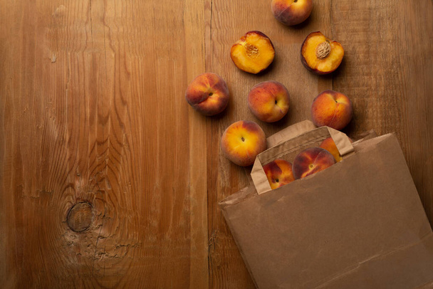 Fresh ripe peaches fruits in paper bag on wooden rustic background. Top view. - Foto, Imagen