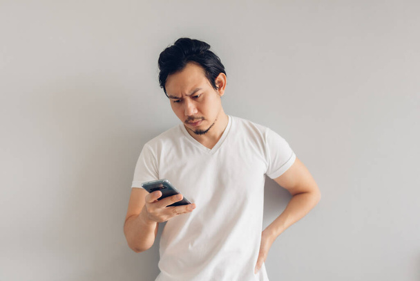 Hombre de pelo largo serio en camiseta casual blanca está utilizando el teléfono inteligente. - Foto, Imagen