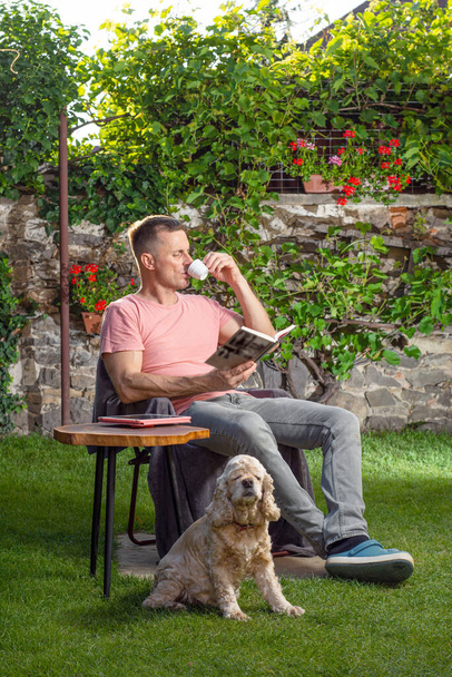 Hombre sentado en una silla y disfrutando de una taza de café en el jardín - Foto, imagen