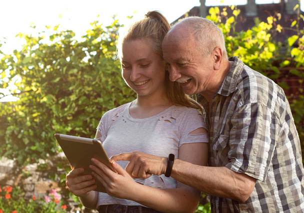 Portrait of happy granddaughter and grandfather using digital tablet outdoors - Photo, Image