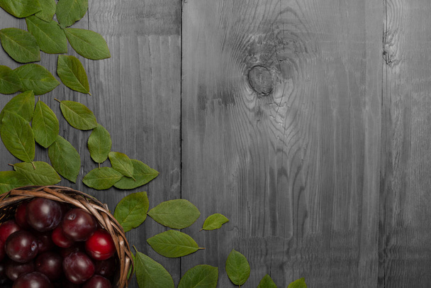 Prunes dans un panier en osier et feuilles sur table en bois noir et blanc. Concept écologique. Vue du dessus
. - Photo, image