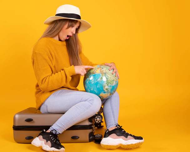 portrait happy woman, traveler with a globe and suitcase, on yellow background - Foto, Imagen