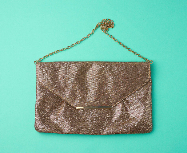 rectangular golden leather fashion clutch on a metal chain on a green background, top view - Photo, Image