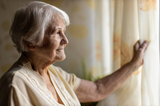 Oudere vrouw die thuis uit het raam kijkt - Foto, afbeelding
