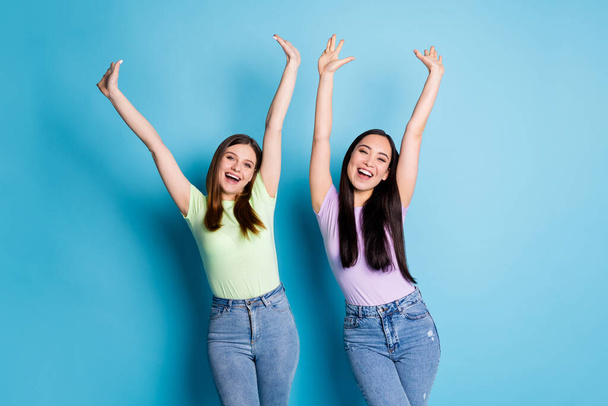 Photo of cheery attractive funny crazy ladies lesbians couple raise arms up overjoyed education achievement college groupmates wear casual t-shirts jeans isolated blue color background - Foto, Bild