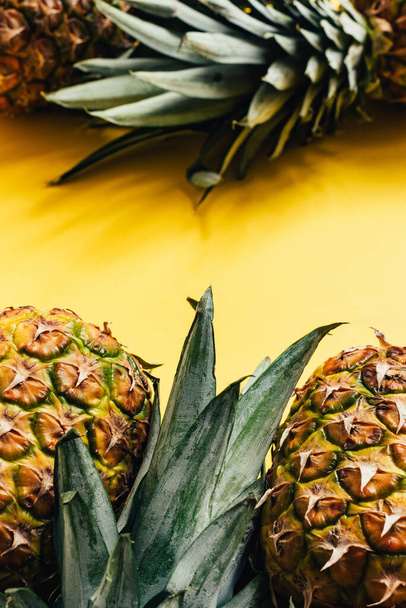 selective focus of fresh ripe pineapples with green leaves on yellow background - Foto, Bild