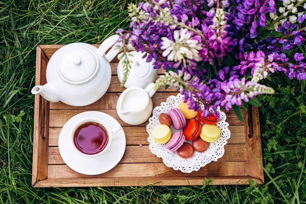 新鮮な空気の中で居心地の良い朝食。梅の花の花瓶、ティーポット、コーヒーティーカップ、木製のトレイにマカロンとケーキ。母の日または女の日。柔らかい選択的フォーカス. - 写真・画像