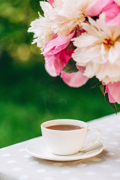Um pequeno-almoço romântico acolhedor ao ar livre. Um vaso de flores de peônias, uma xícara de chá de café na mesa. Foco seletivo suave
. - Foto, Imagem