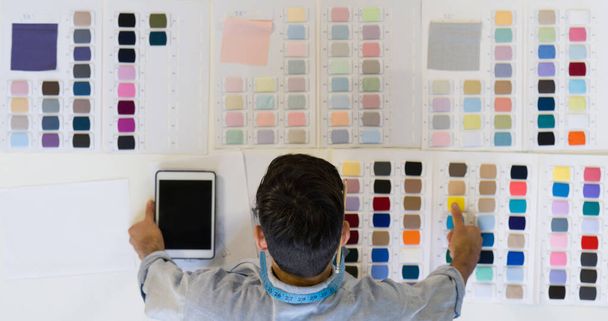 Joven diseñador de moda elegir el color de la tela que se utilizará con el diseño en una mesa llena de muestras de tela de colores brillantes. Ambiente matutino en la sastrería. (Vista superior
) - Foto, Imagen