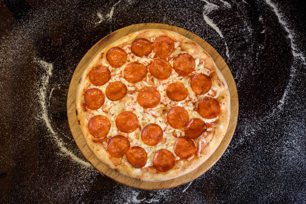 Top view of pepperoni pizza on the black background with spilled flour. - Foto, imagen