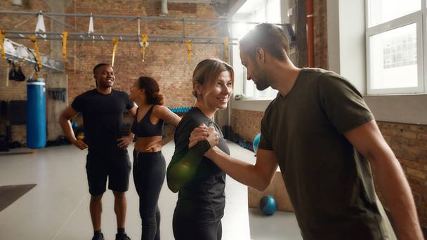 We believe in each other. Group of sportive people in black sportswear standing at industrial gym. Man and woman trying arm wrestilng playfully. Group training, teamwork concept - 写真・画像