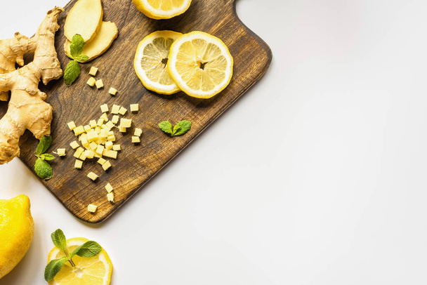 top view of ginger root, lemon and mint on wooden cutting board on white background - Foto, afbeelding