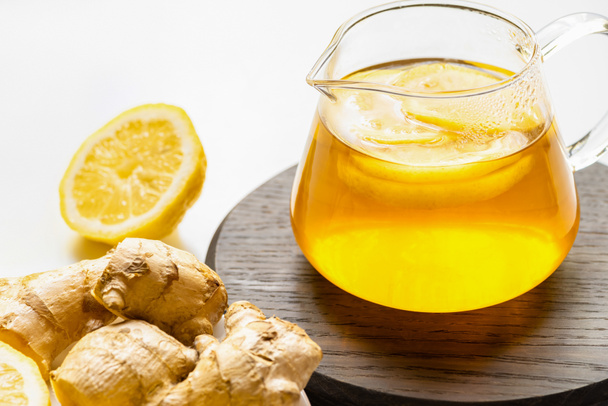 hot tea in teapot on wooden board near ginger root, lemon on white background - Fotó, kép