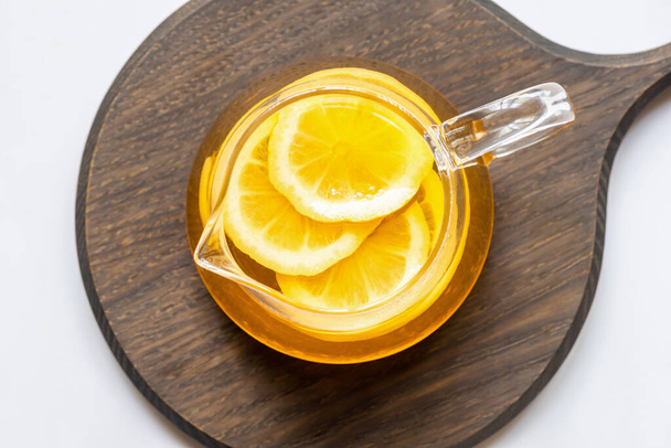 сверху вид на горячий чай с ломтиками лимона на деревянной доске на белом фоне
 - Фото, изображение