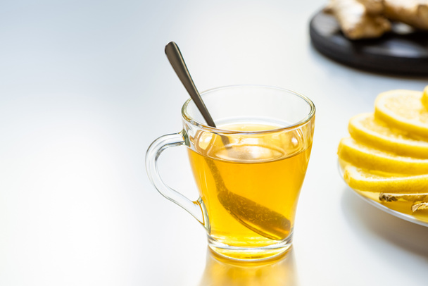 foco selectivo de té caliente en taza de vidrio con cuchara cerca de rodajas de limón sobre fondo blanco
 - Foto, imagen