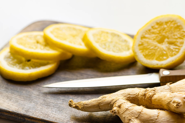 selective focus of hot ginger root, lemon on wooden cutting board with knife on white background - 写真・画像